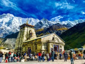 a group of people outside Kedarnath Temple with snow covered mountains in the background